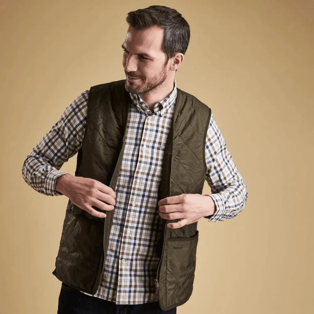 Doublure Polarquilt Olive portée ouverte sur une chemise à carreaux, fond beige