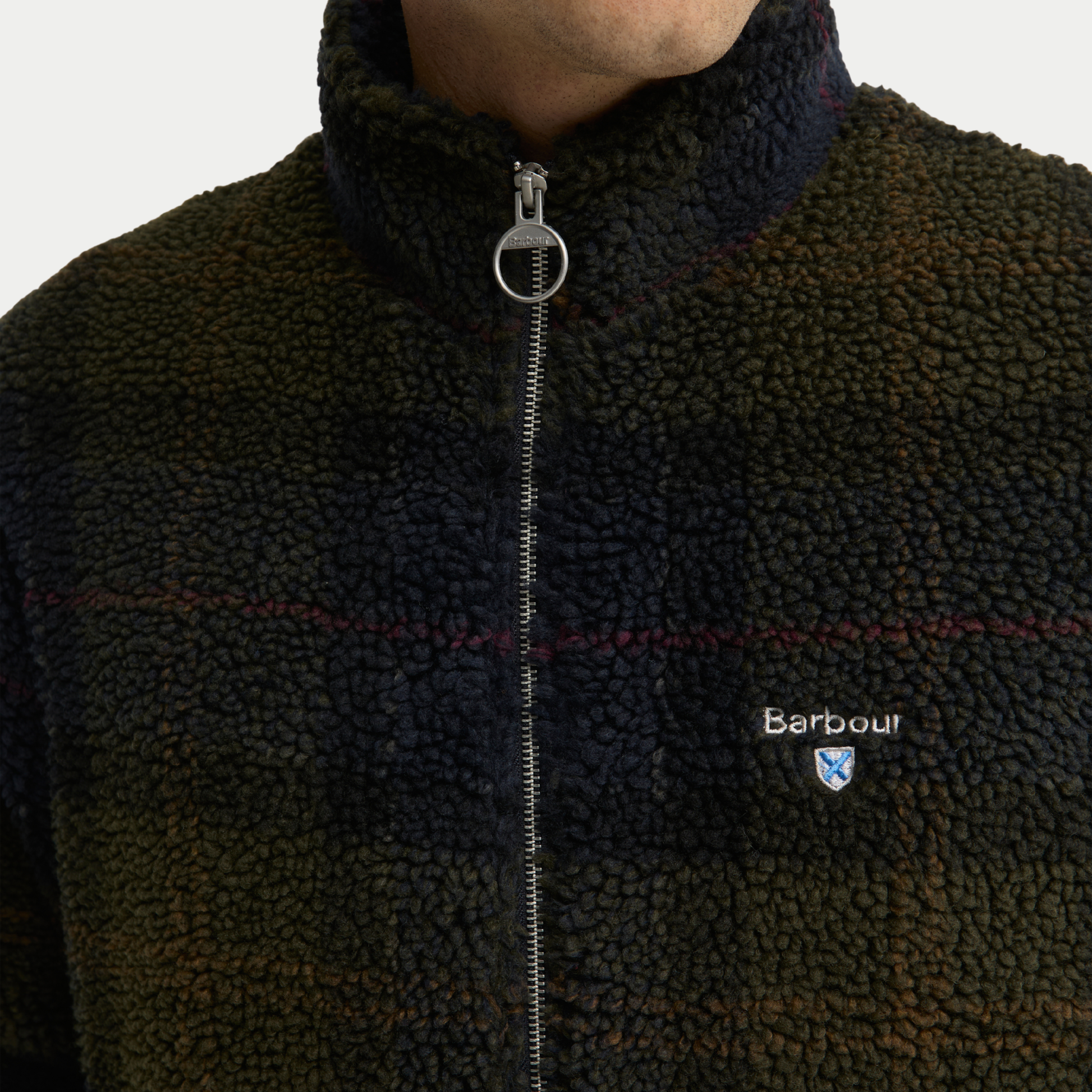 Détail du sherpa bouclé tartan olive foncé, filets rouges et tirette anneau métal Barbour