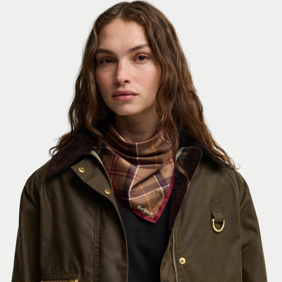 Foulard Kinsale tartan marron noué en bandana au cou, ouvert sur le col en velours d'une veste cirée olive