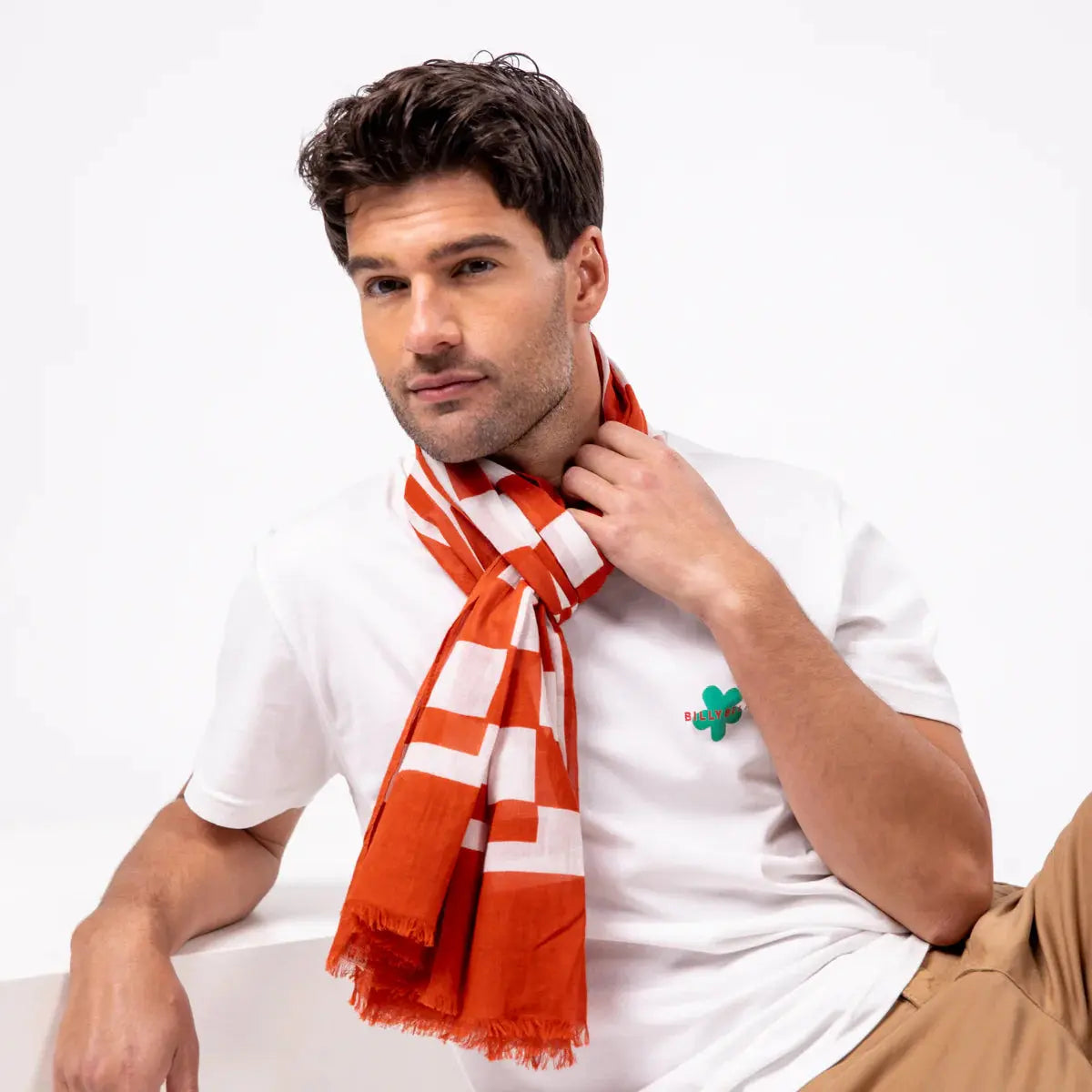 Foulard à blocs blancs sur fond orange brique noué court au cou, les pans frangés le long du buste