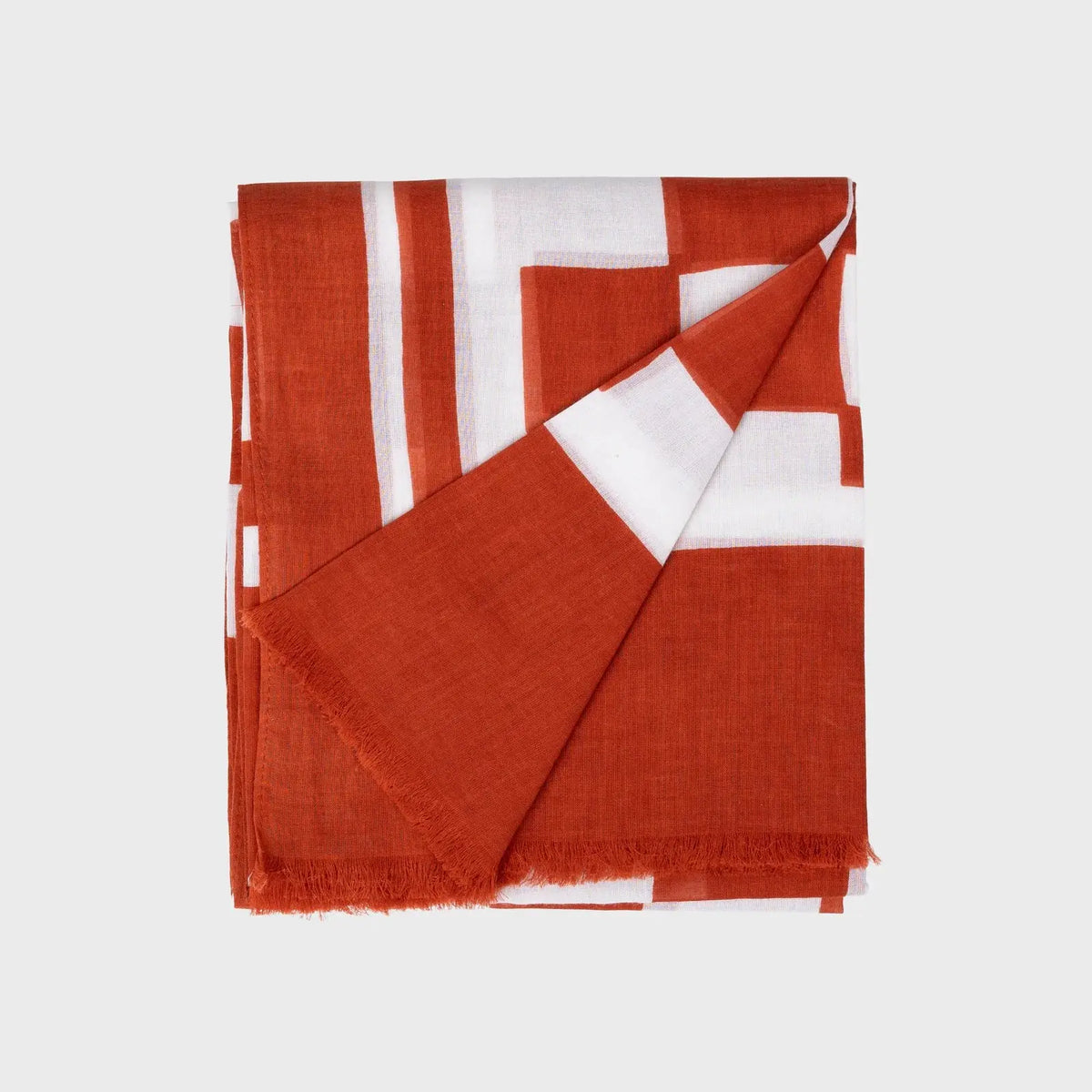 Foulard en coton plié, motif géométrique de blocs blancs décalés sur fond orange brique, bords frangés