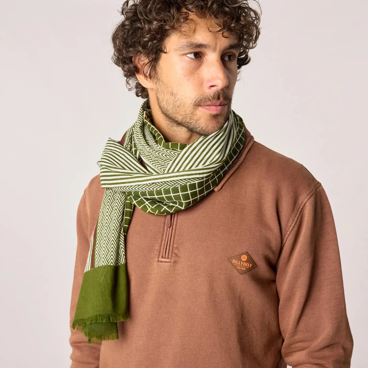 Foulard imprimé vert olive à motifs mêlés noué au cou, pan uni frangé descendant le long du buste