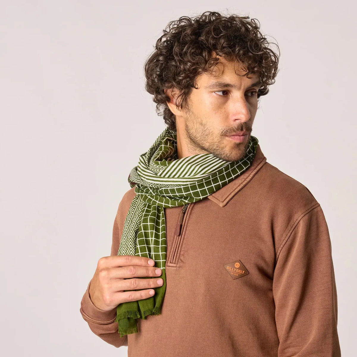 Foulard vert olive porté en écharpe, bloc uni frangé et liseré bordeaux visibles sur le pan avant