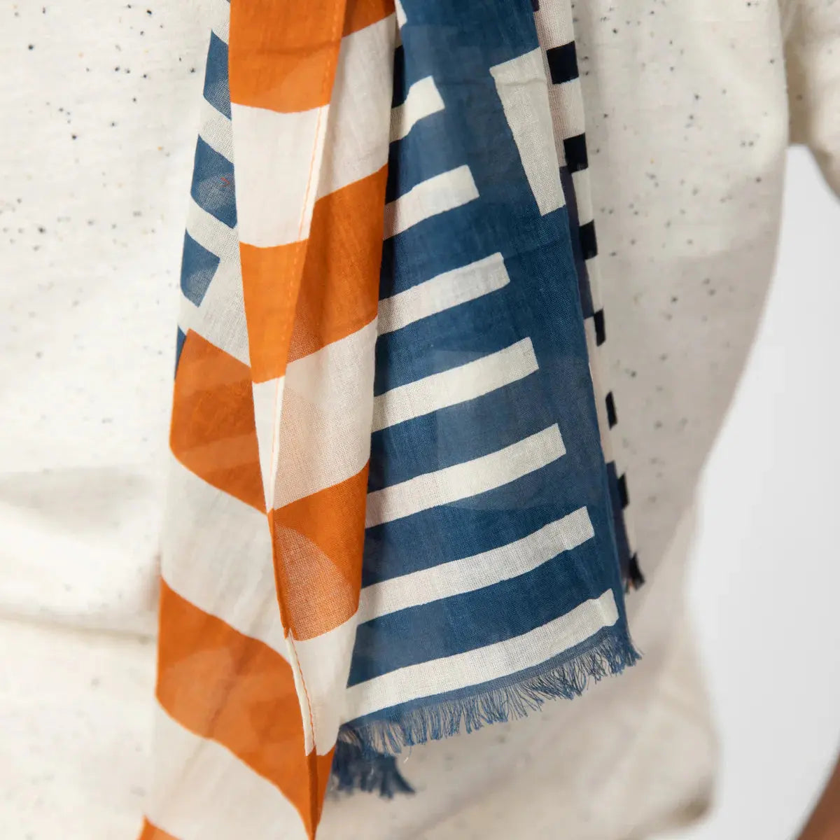 Les deux pans côte à côte : face orange rouille rayée, face bleu jean et franges en bas du foulard