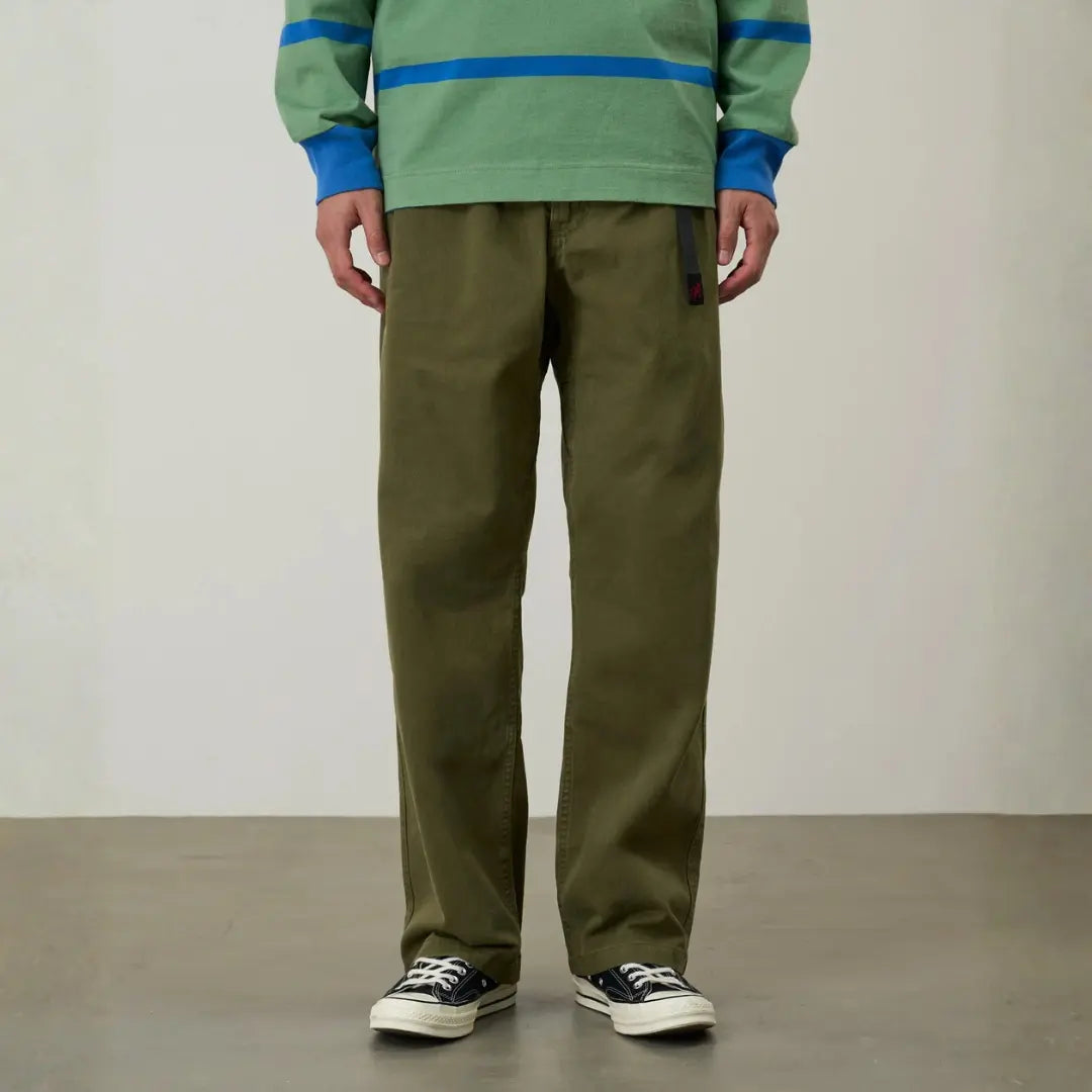 Gros plan porté du G-pant olive : taille froncée, sangle anthracite à boucle, patch logo rouge et jambe droite