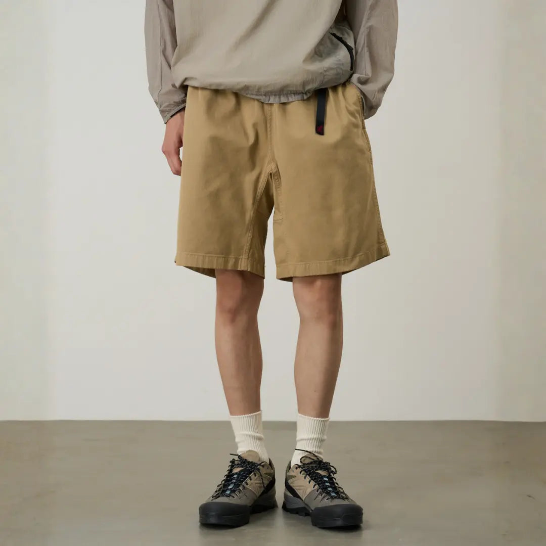 G-short beige chino porté de près : sangle noire à boucle, patch logo rouge et large jambe au-dessus du genou