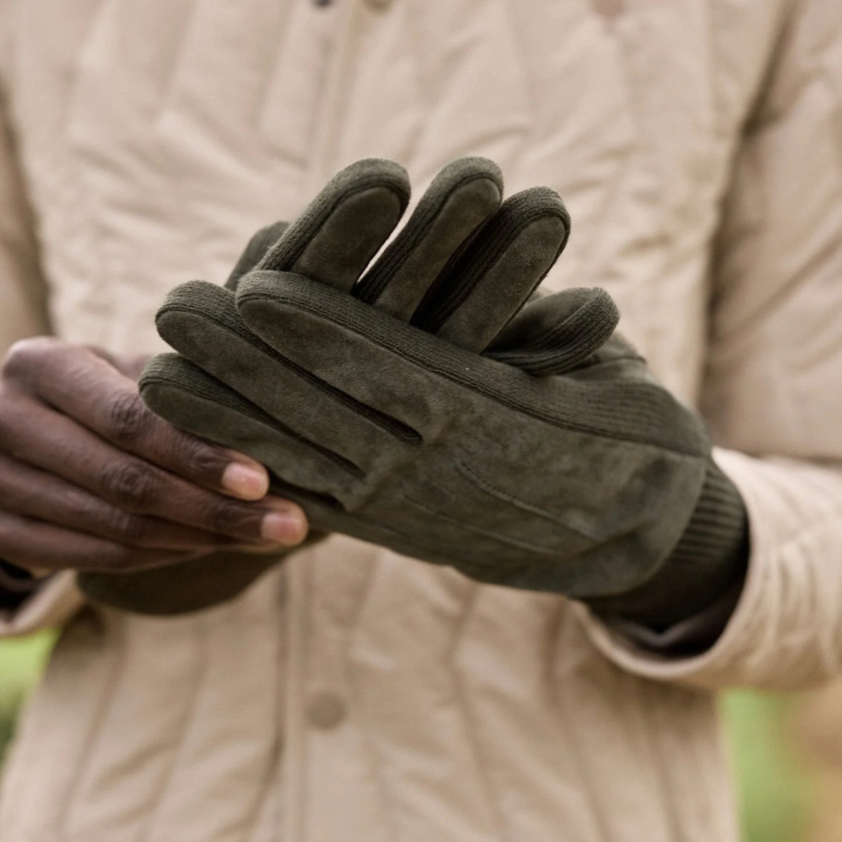 Gant Faguo en nubuck kaki enfilé à la main devant une veste matelassée beige, poignet tricot visible