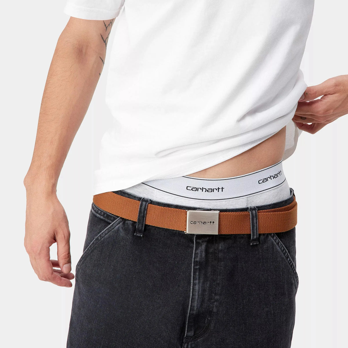 Ceinture élastique blanche du boxer porté, visible au-dessus d'un jean gris et d'une sangle camel