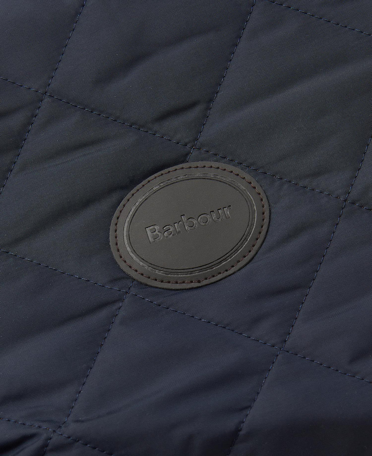 Macro du patch cuir ovale Barbour sur le matelassage losange bleu marine