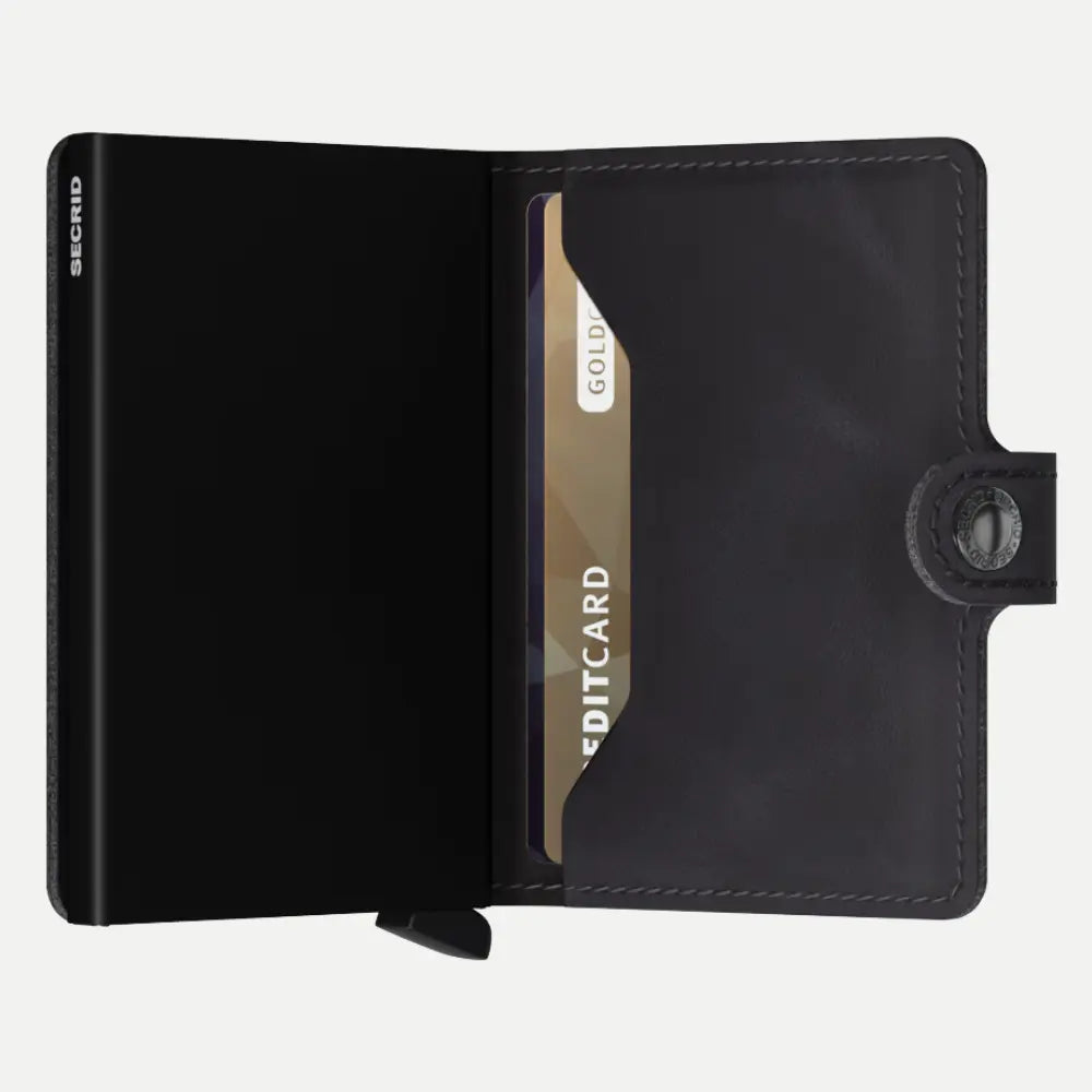 Portefeuille en cuir noir patiné ouvert, boîtier noir et carte dorée dans le rabat