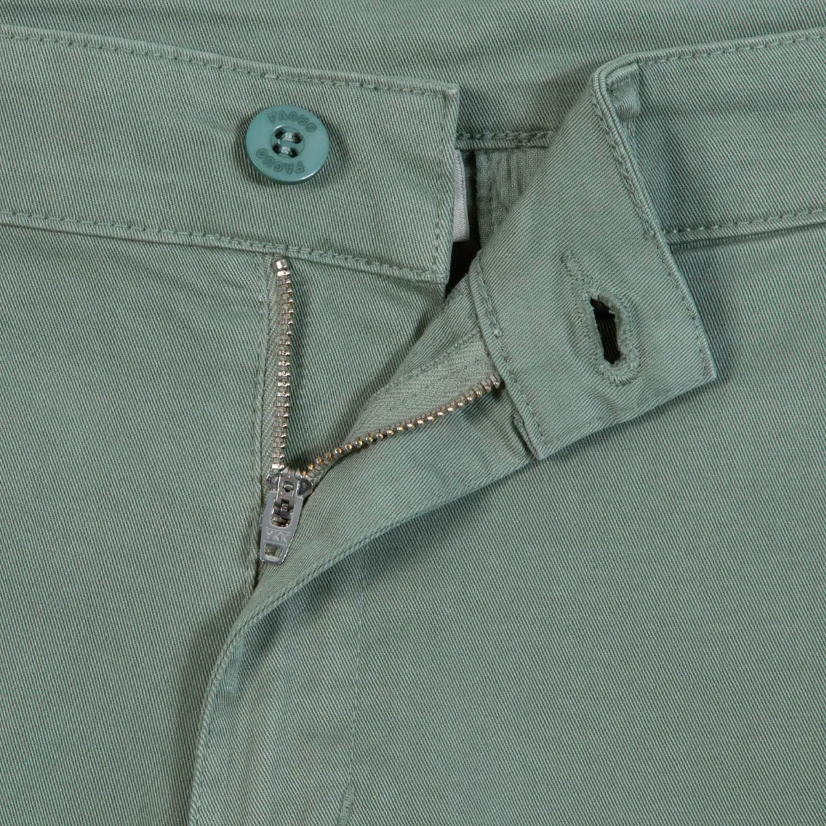 Détail de la taille du Brix : bouton gravé, braguette zippée et sergé vert clair
