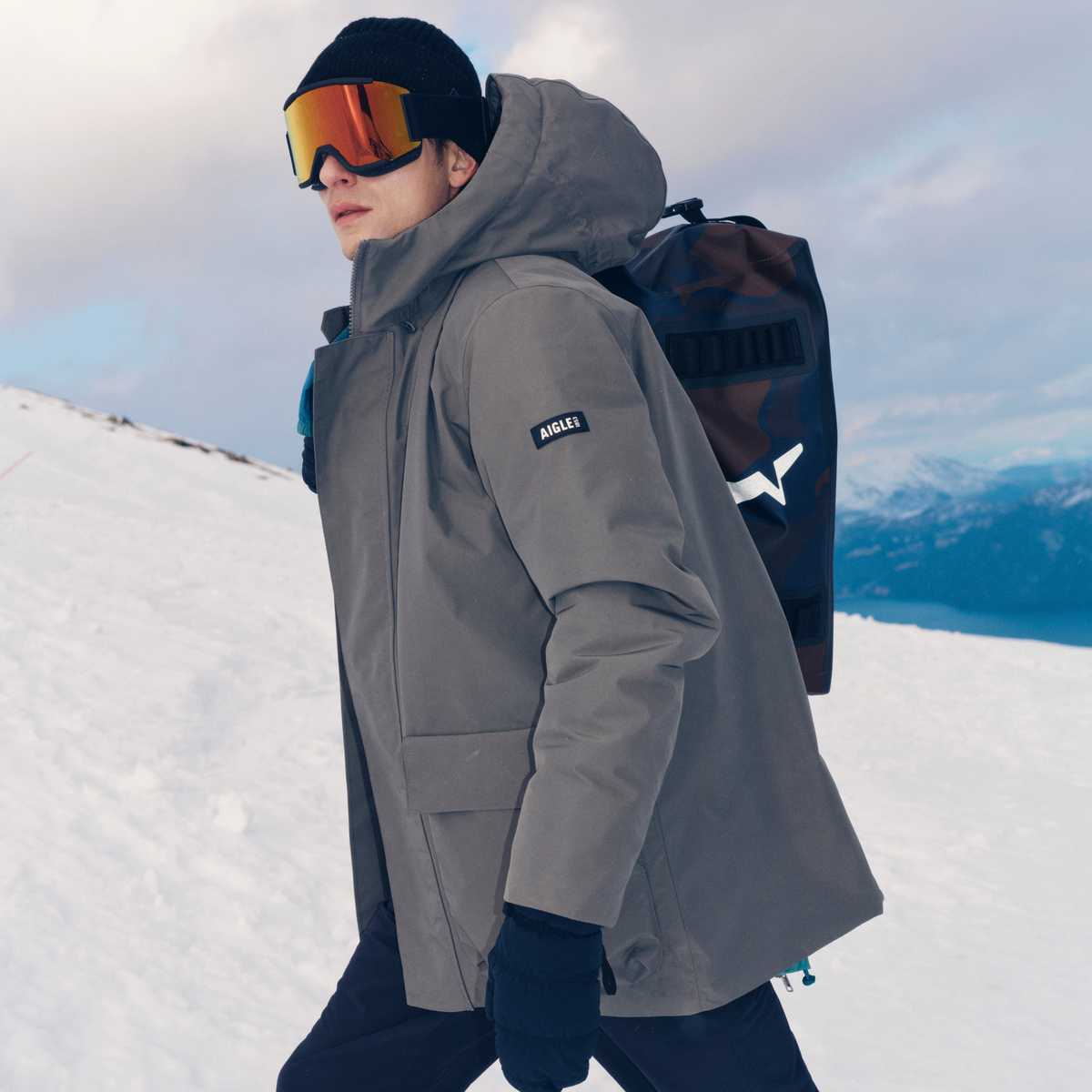 Parka matelassée grise portée en extérieur dans la neige, capuche relevée