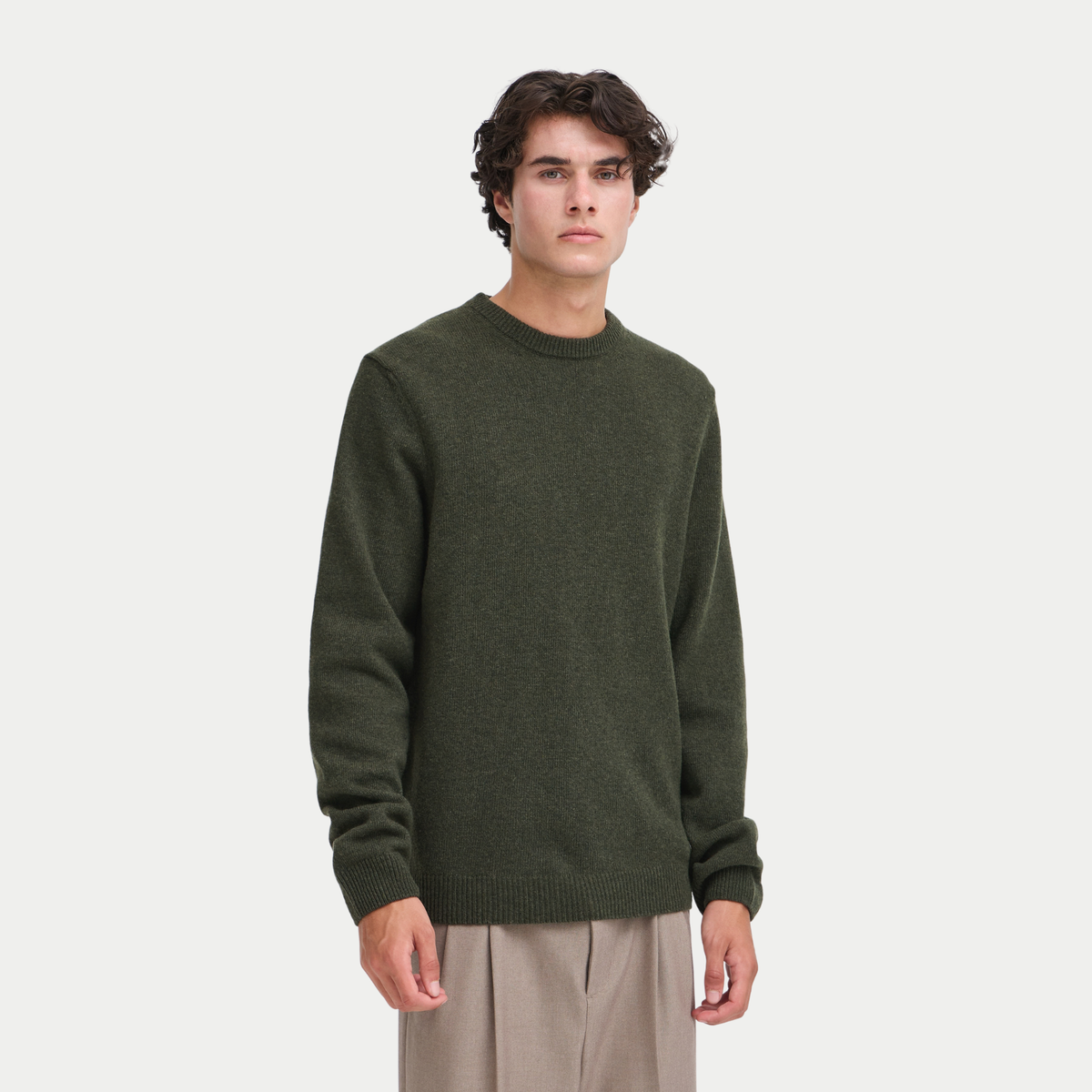 Pull col rond kaki foncé porté de face, coupe droite en laine d'agneau, pantalon beige
