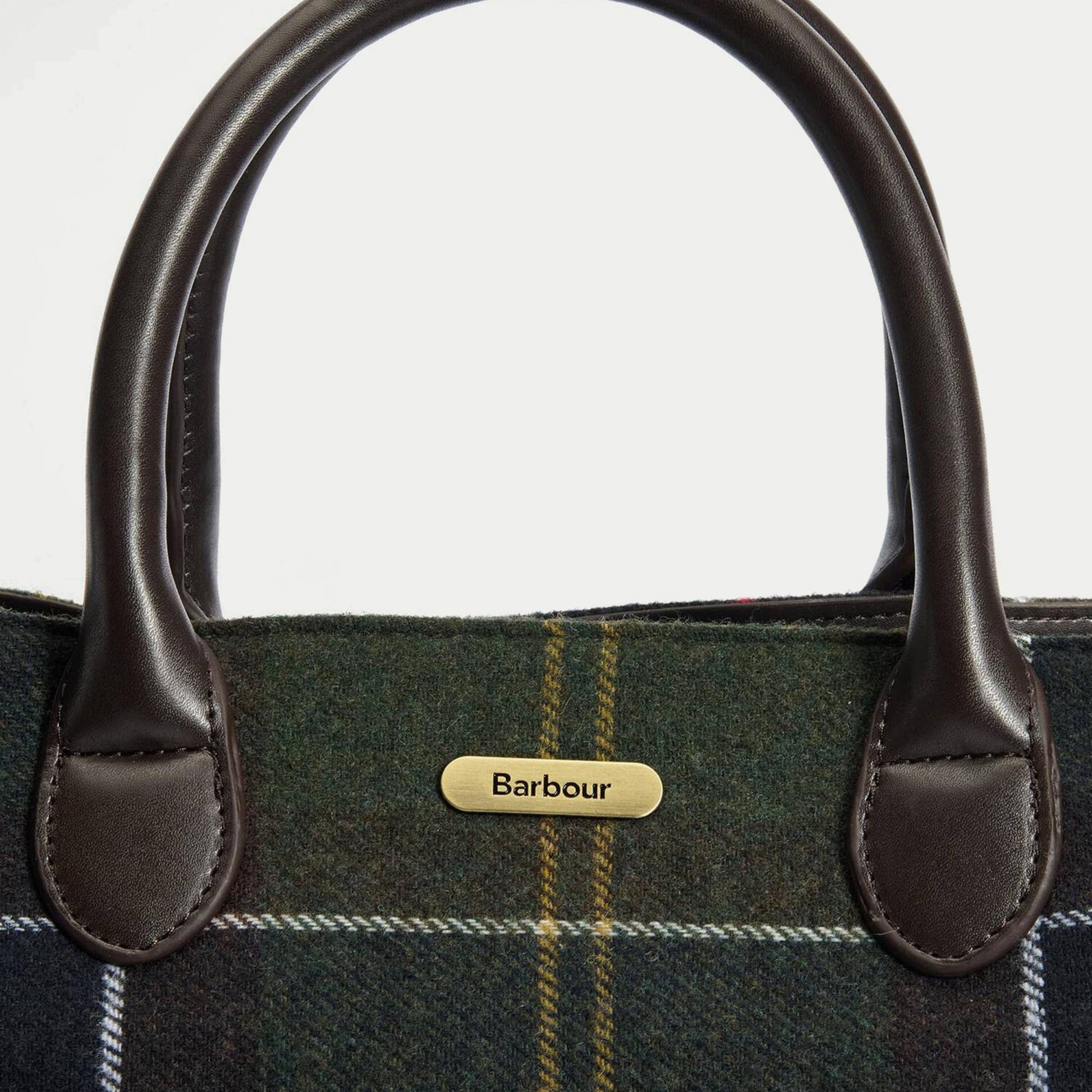 Macro de la plaque logo Barbour en laiton brossé posée sur le tartan olive du tote bag Barrhill