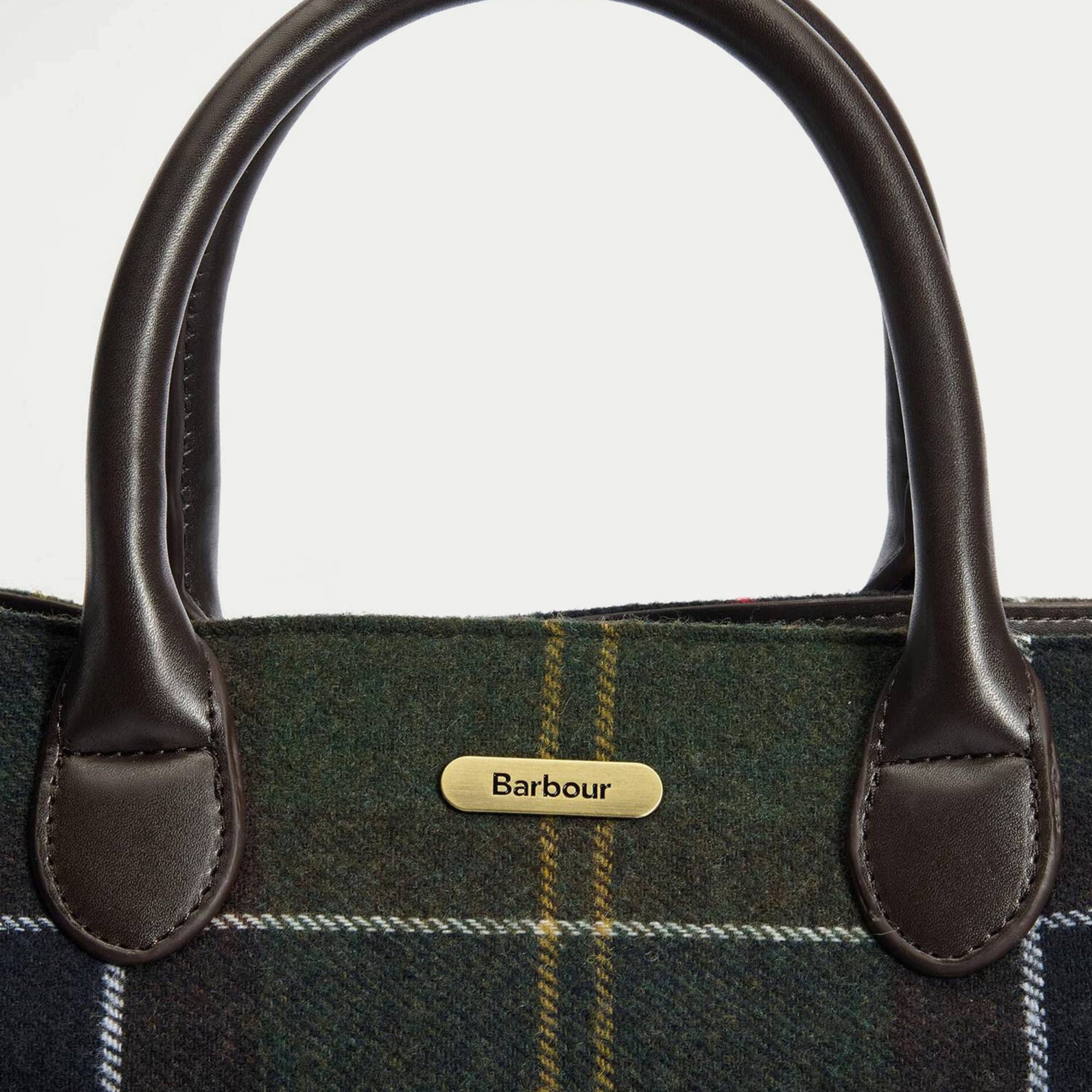 Macro de la plaque logo Barbour en laiton brossé posée sur le tartan olive du tote bag Barrhill