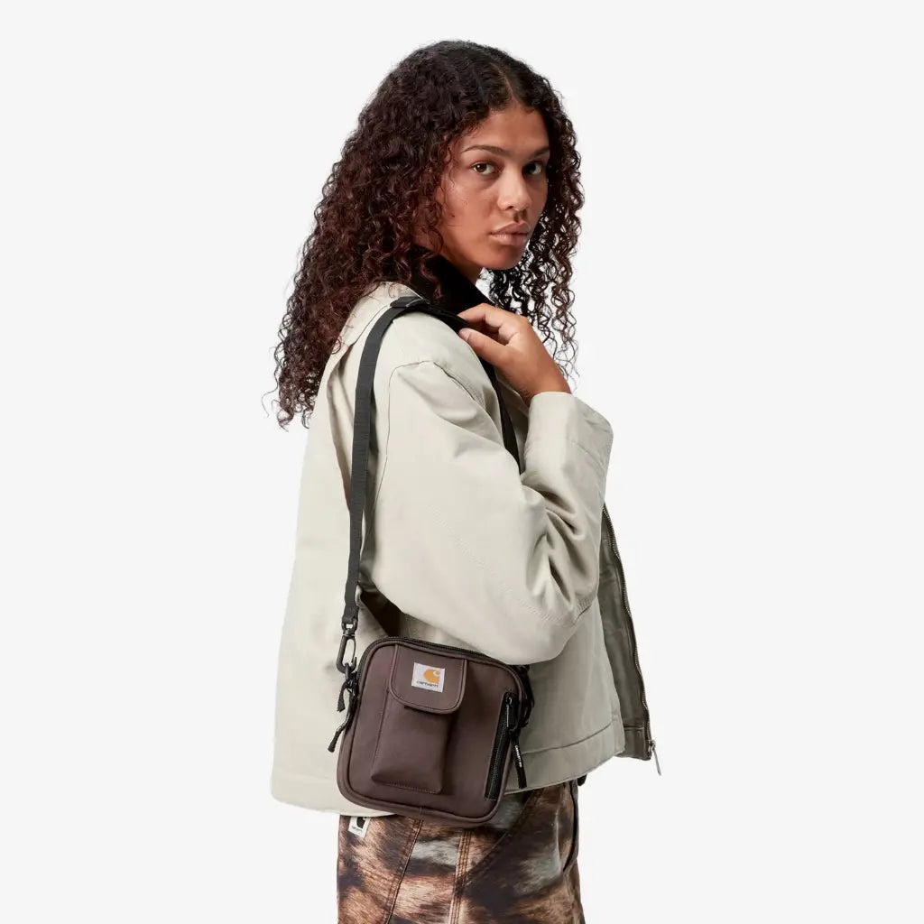 Sacoche Essentials Bag Palisander brun bordeaux Carhartt WIP portée en bandoulière sur la hanche, vue de trois-quarts dos