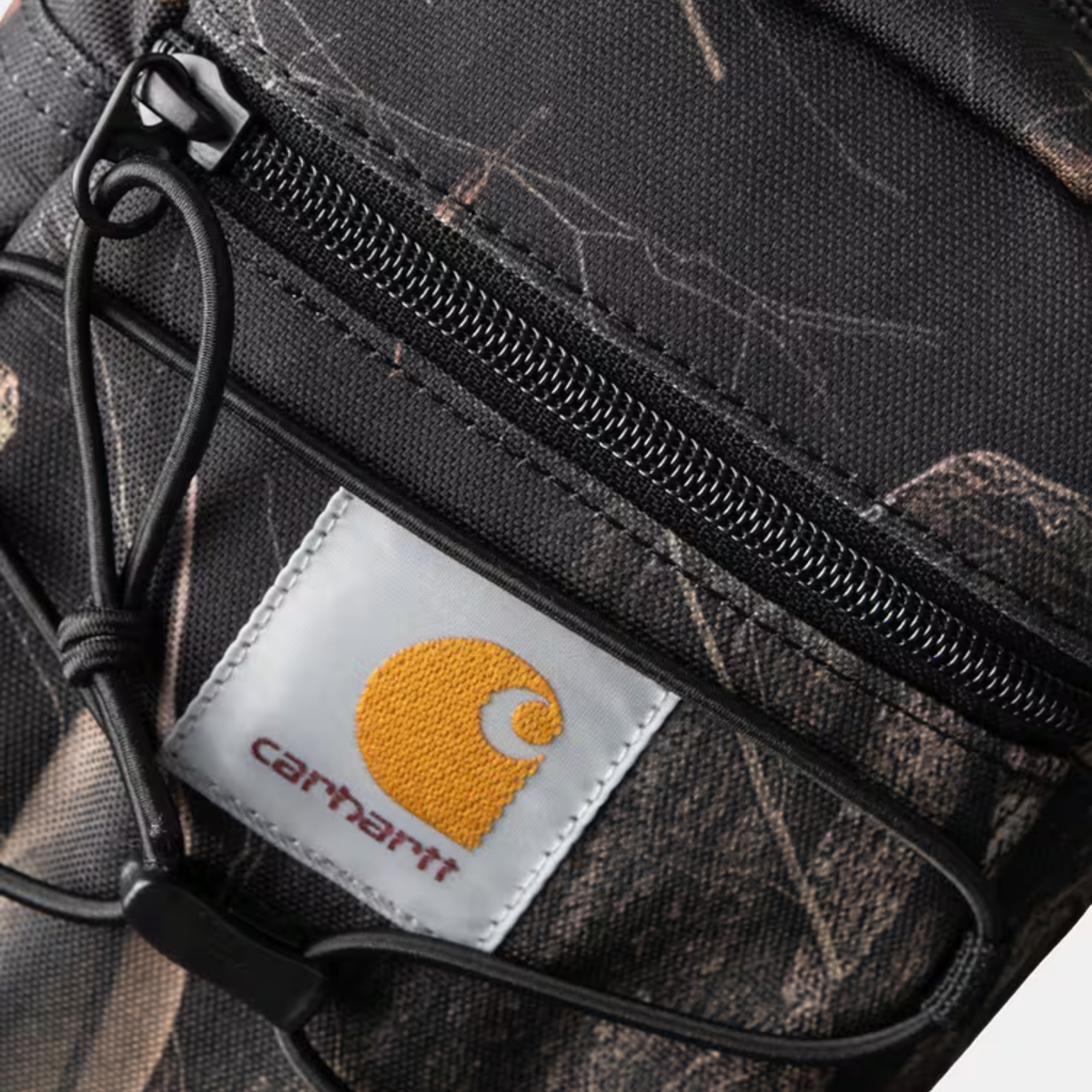 Détail du camouflage Feather Tree sur la sacoche Kickflip Carhartt WIP : écorces et branches imprimées, zip et Square Label tissé