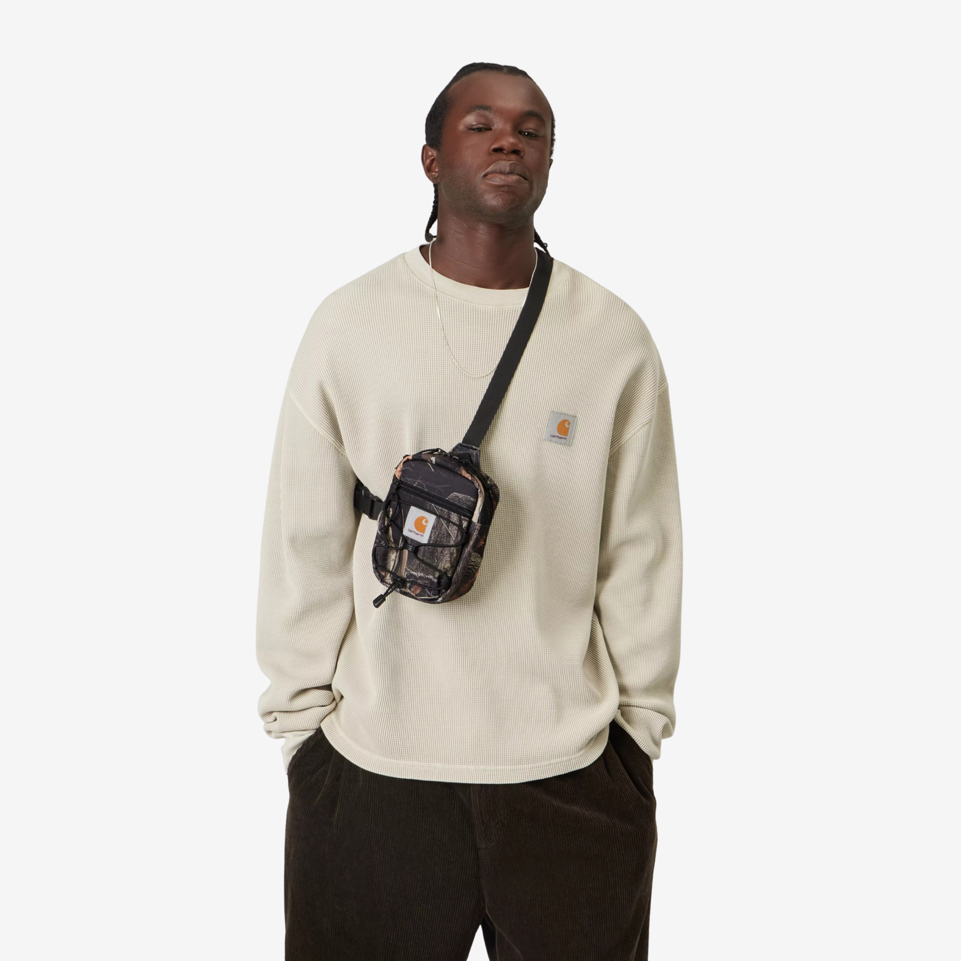 Sacoche Kickflip Carhartt WIP Camo Feather Tree portée en travers de la poitrine sur un sweat écru