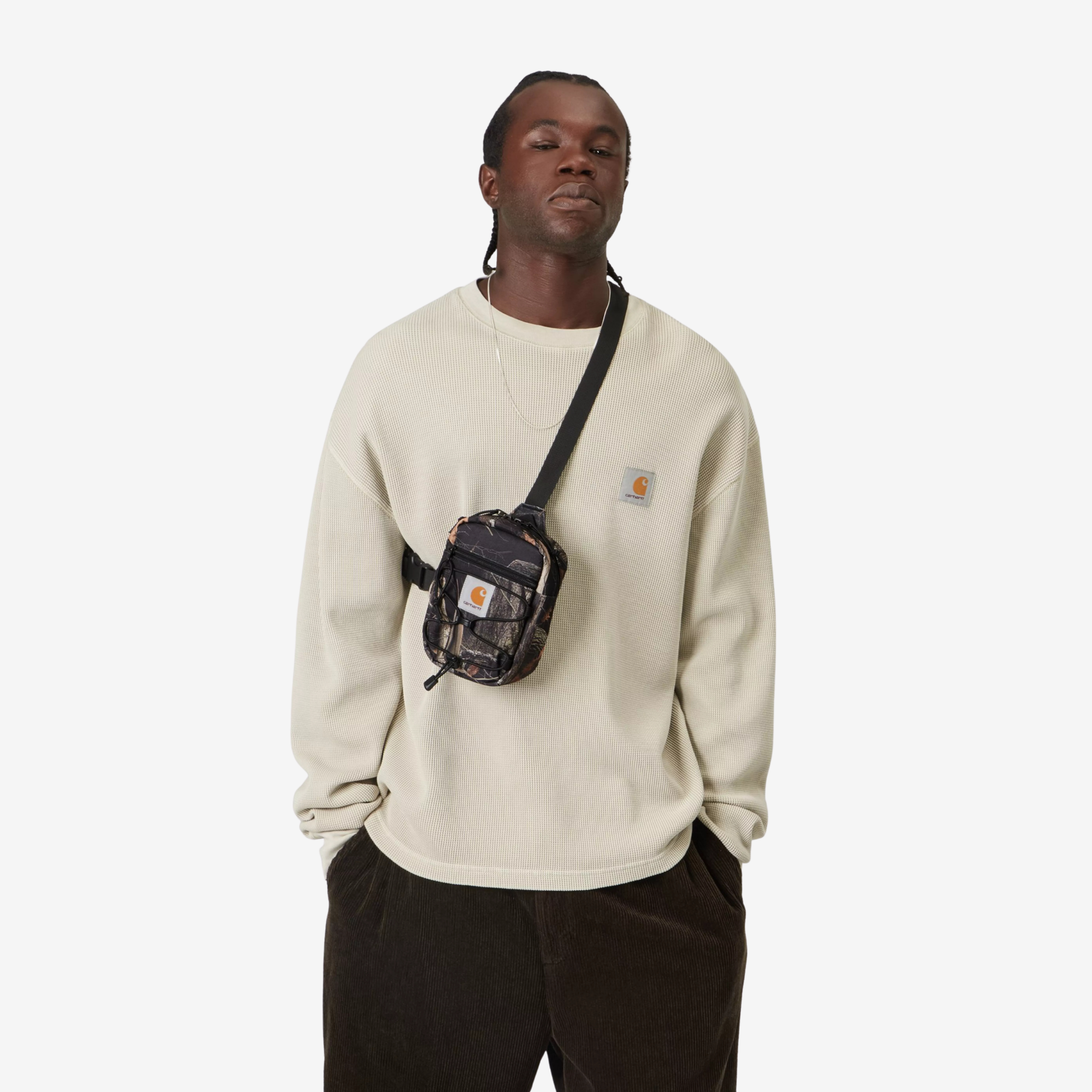 Sacoche Kickflip Carhartt WIP Camo Feather Tree portée en travers de la poitrine sur un sweat écru