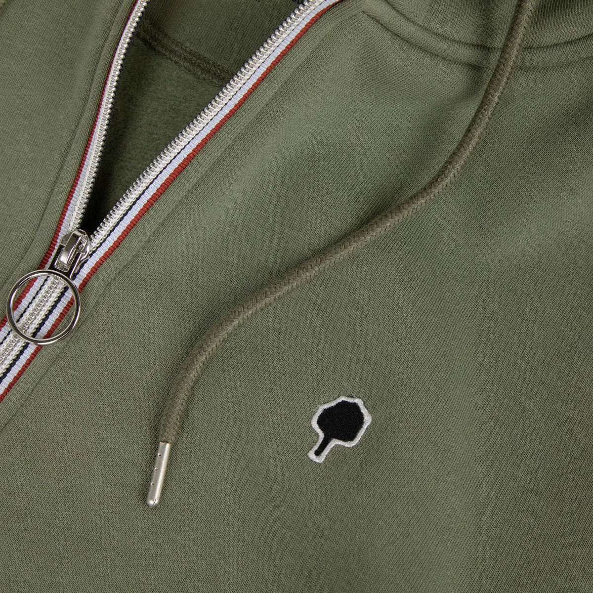 Gros plan sur le curseur à anneau métal, le ruban de zip tricolore et l'arbre brodé noir du sweat kaki