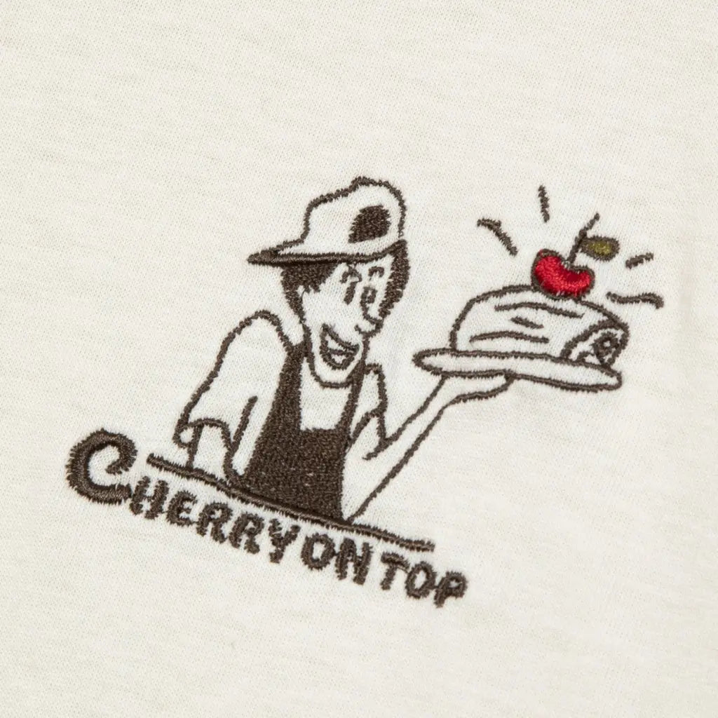Macro de la broderie Cherry on Top : pâtissier, gâteau et cerise rouge sur coton écru