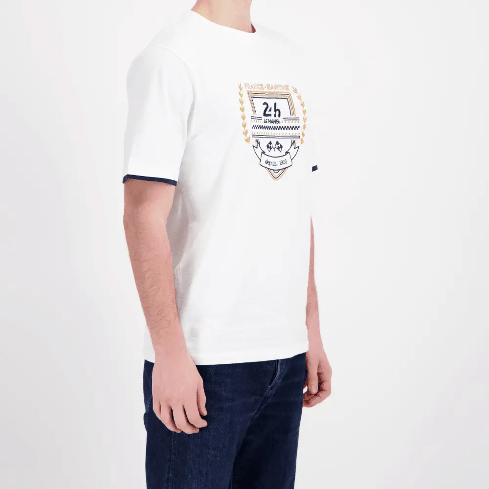 T-shirt blanc porté de trois quarts, écusson brodé sur le buste et liseré bleu marine au bas des manches