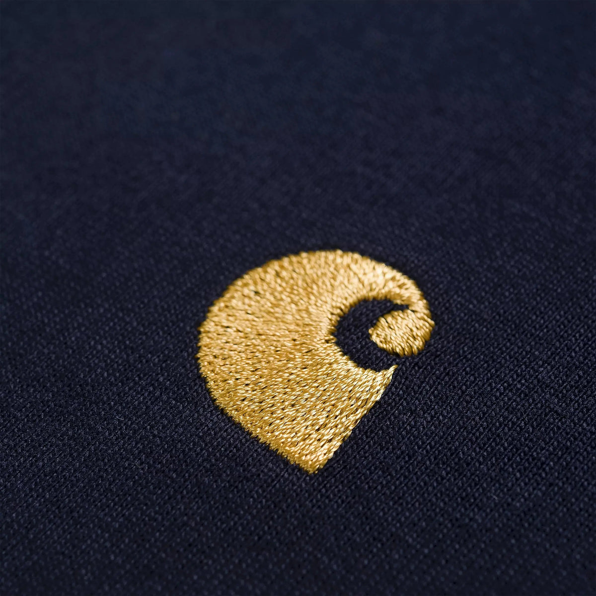 Gros plan sur le logo C Carhartt brodé doré et le jersey de coton bleu marine du T-shirt Chase