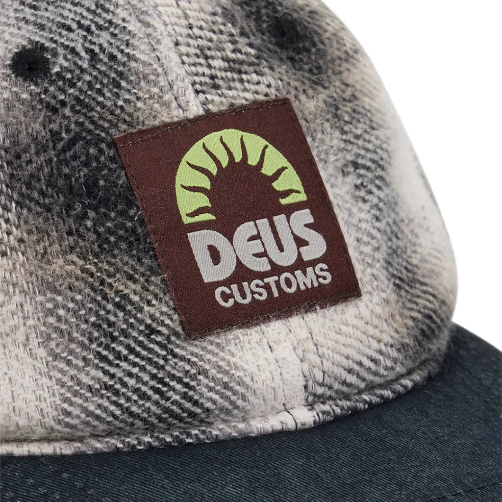 Gros plan du patch tissé bordeaux au soleil vert anis sur la flanelle de la Vacay Check Cap