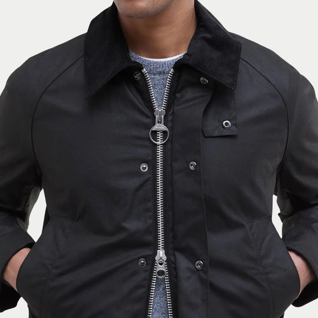 Zip argenté à anneau et col en velours côtelé de la veste Ashby noire, portée sur un pull