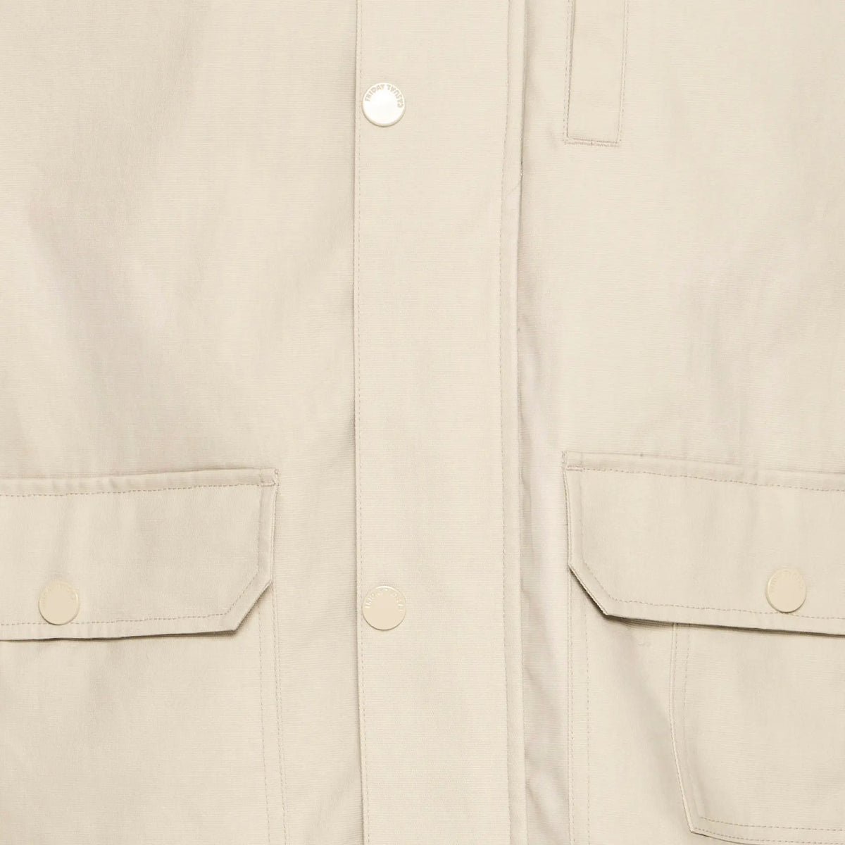 Détail du coton ciré beige, pressions gravées, poche poitrine passepoilée et poches à rabat