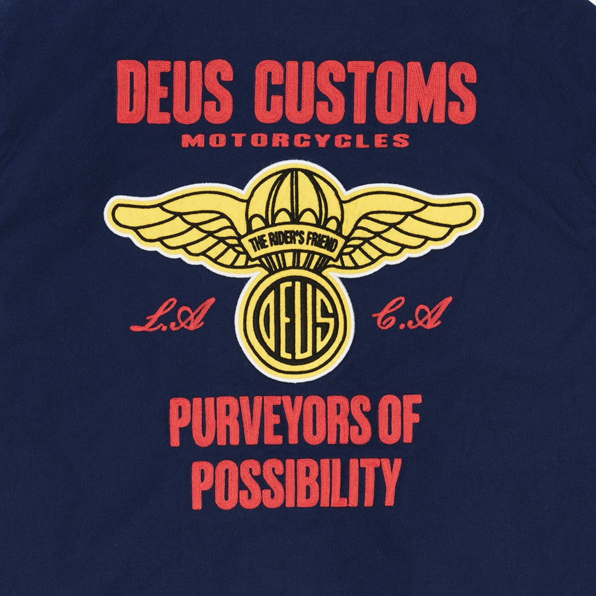 Gros plan du dos de la Veste Cutaway Bleu Marine Deus Ex Machina : broderie chaînette rouge et écusson ailé The Rider's Friend