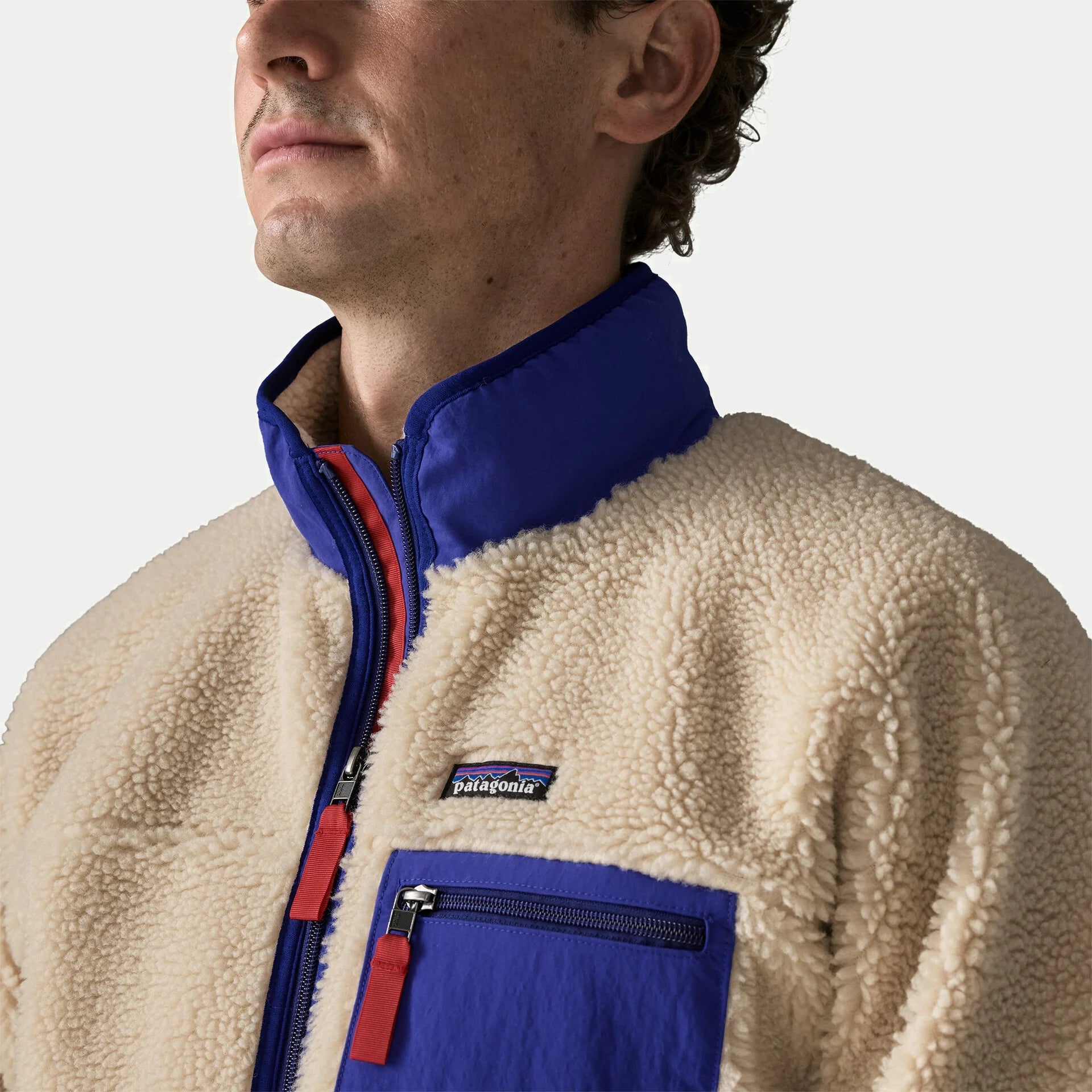Détail du col montant nylon cobalt et de l’étiquette Patagonia sur la veste polaire Retro-X sherpa écru