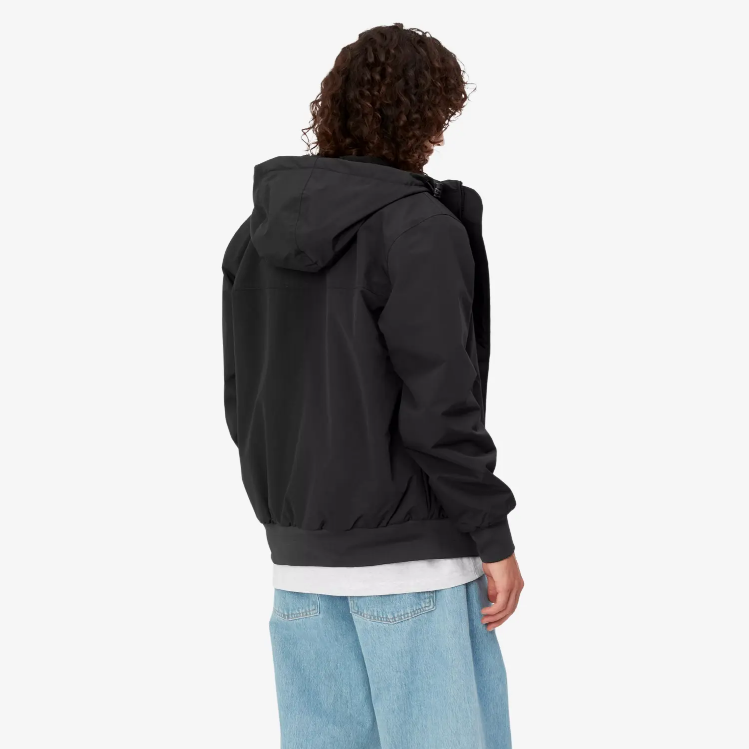 Homme portant la veste Sail Carhartt WIP noire, vue de dos, capuche rabattue et bas en bord-côte