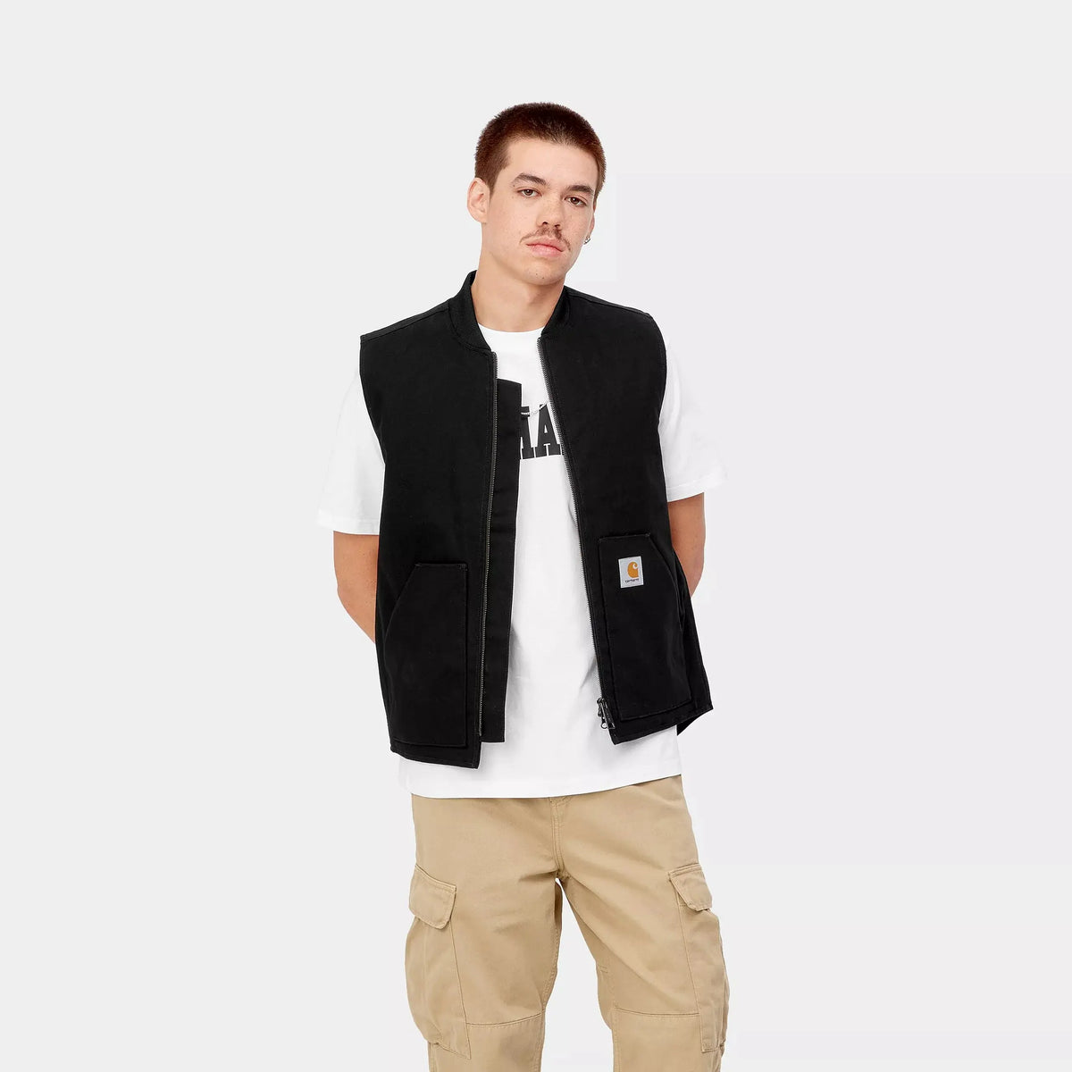 Veste sans manches noire portée ouverte sur un t-shirt blanc, patch Carhartt cousu sur la poche droite