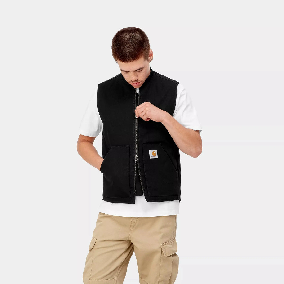 Buste de face, veste sans manches noire portée mi-ouverte, zip central et deux grandes poches plaquées