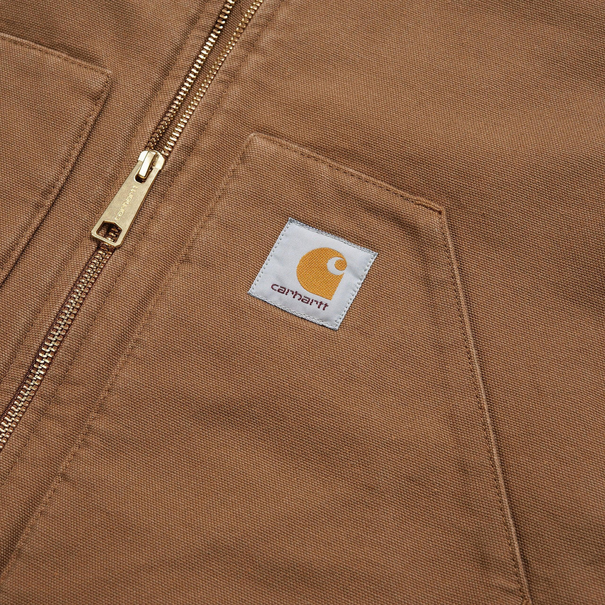 Macro sur la toile brun caramel : patch Carhartt cousu sur la poche et curseur de zip laiton gravé