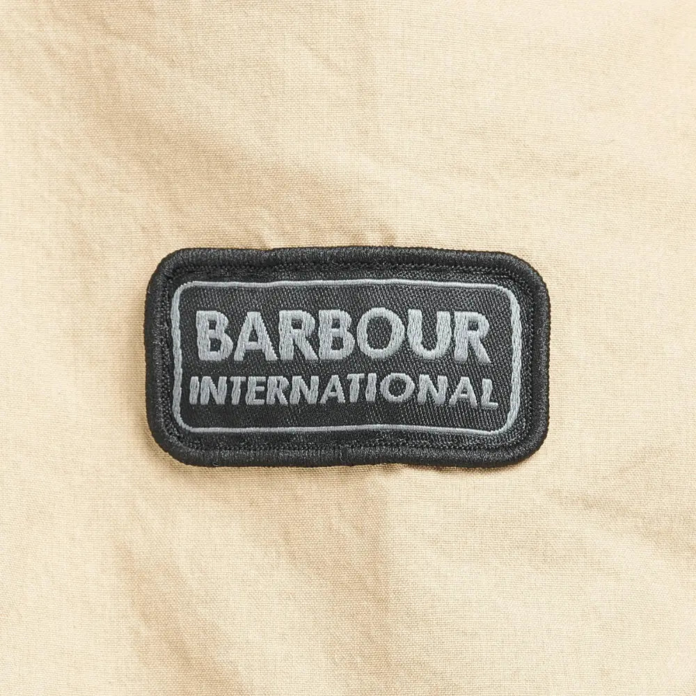 Écusson brodé Barbour International noir et gris cousu sur la manche beige
