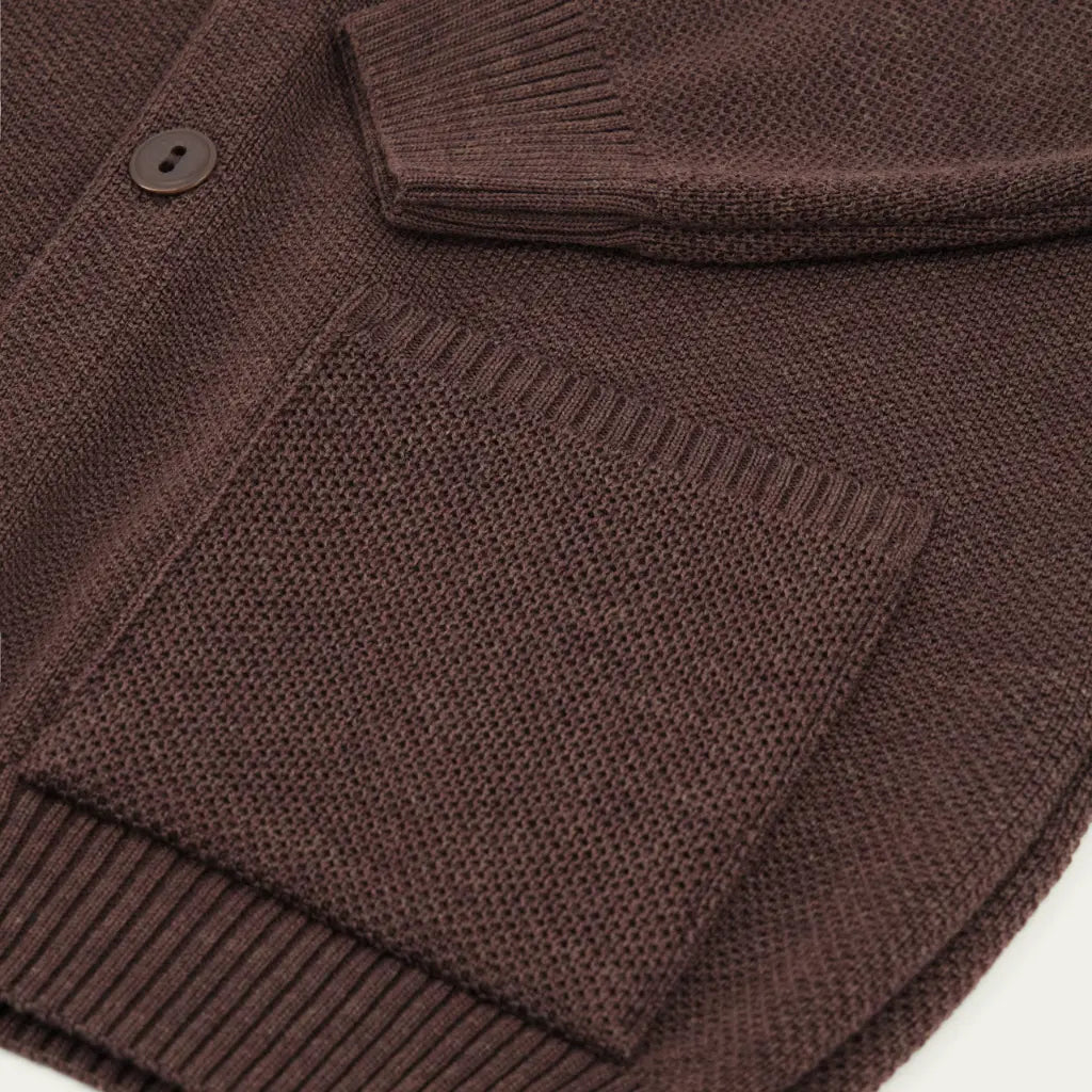 Gros plan d'une poche plaquée du Youri Cardigan marron, bouton foncé et maille au point de riz
